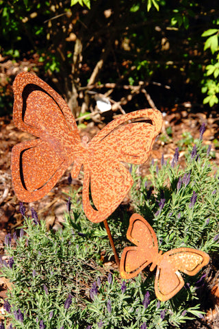 Schmetterlinge aus Rost als Gartenstecker zwischen blühenden Pflanzen